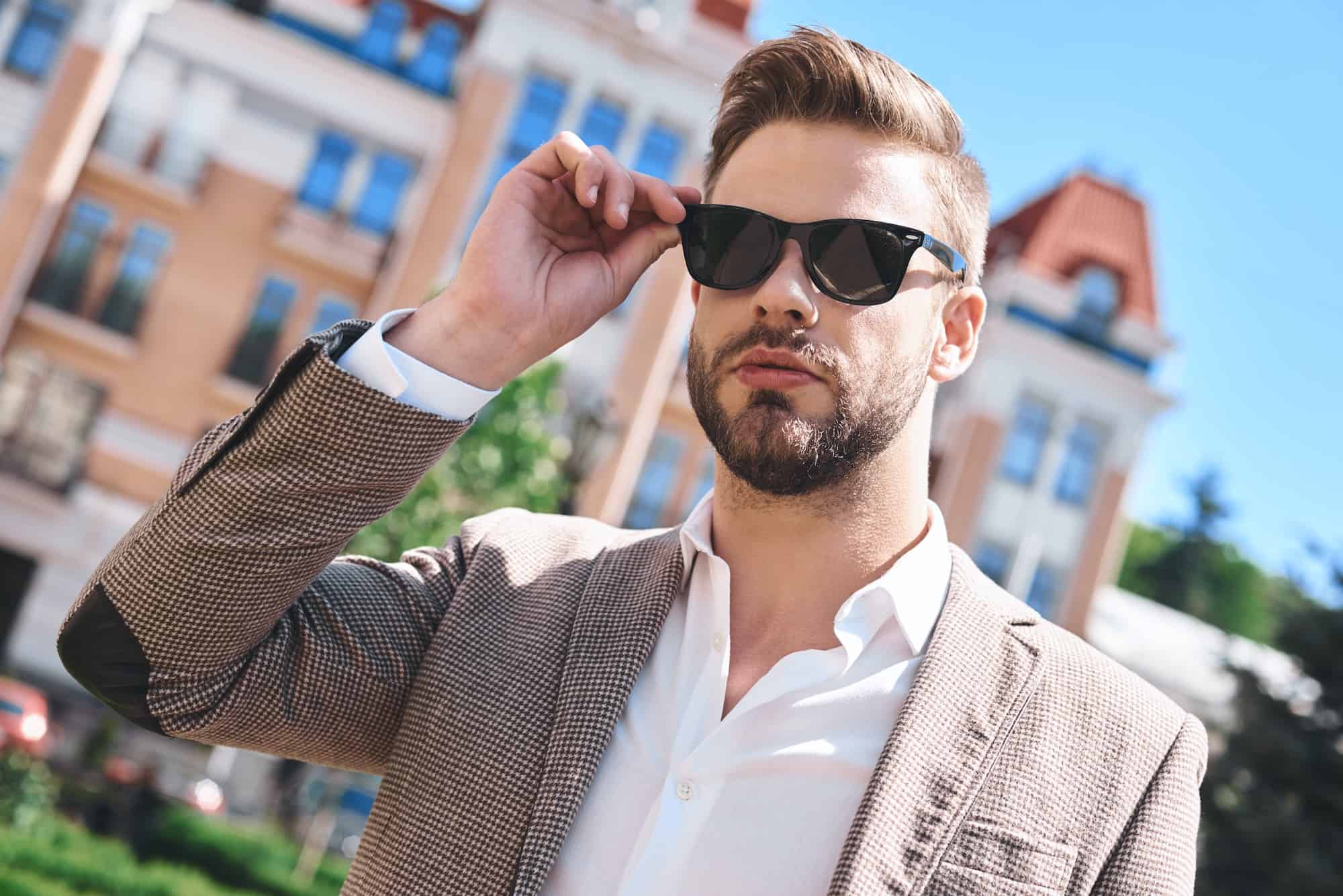 Portrait of a handsome elegant young man, model of fashion, wearing tinted sunglasses in urban